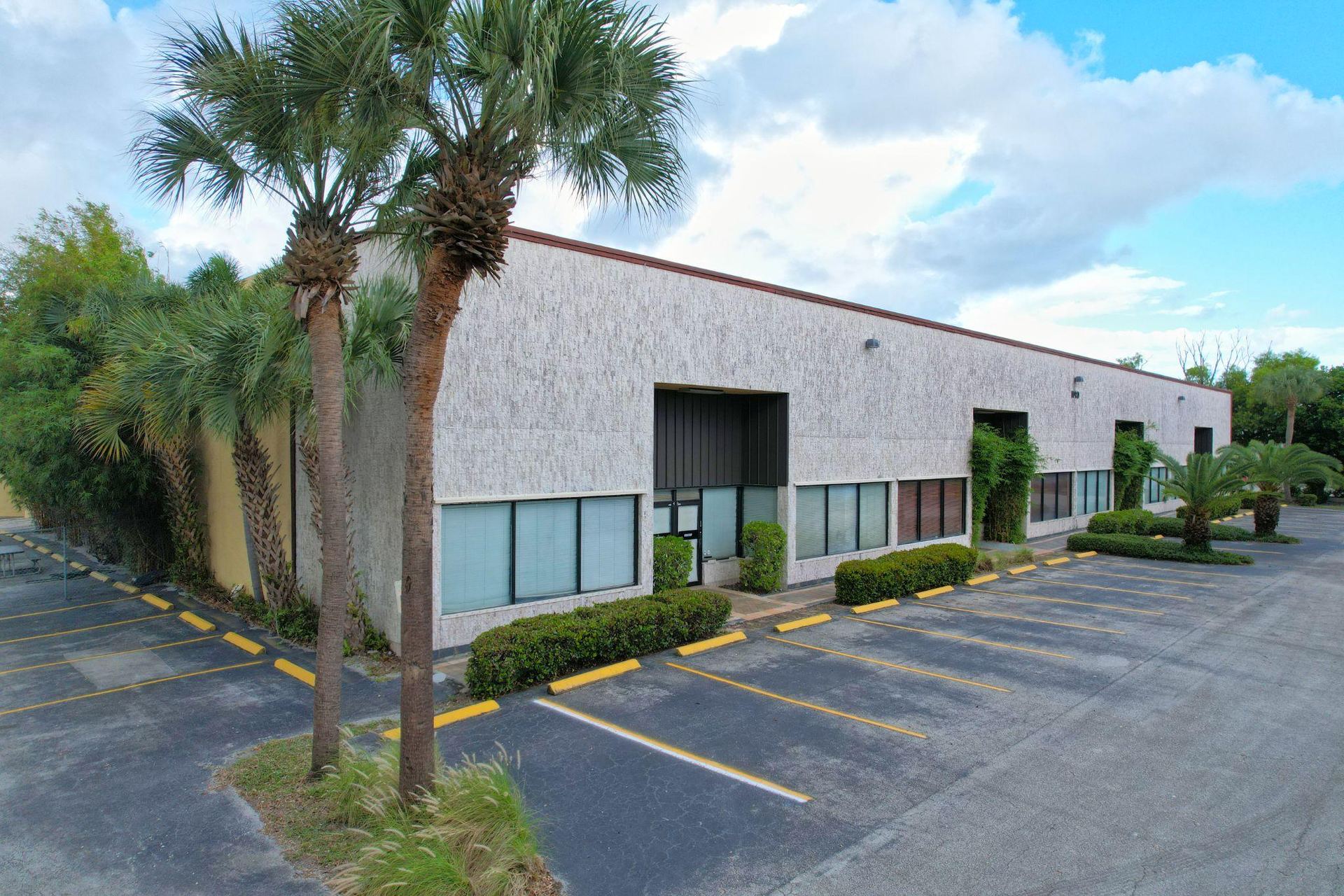 Exterior of the 1190 Stirling Road flex showroom warehouse, with palm trees and a striped parking lot in the foreground