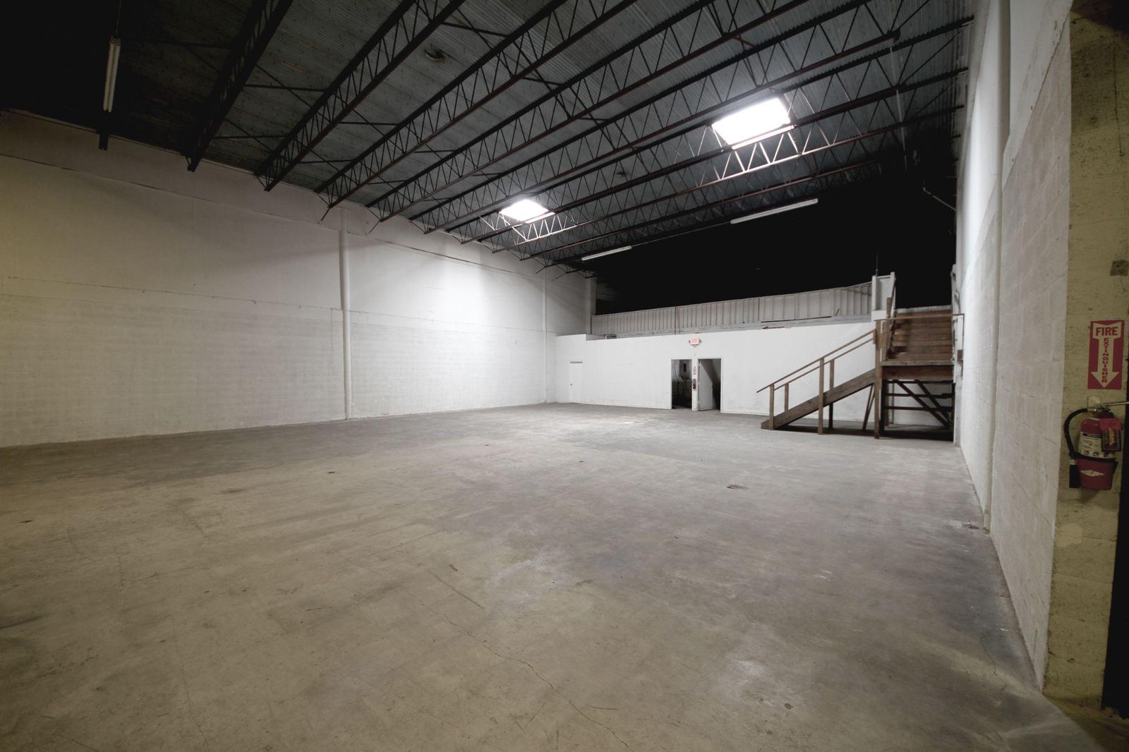 Warehouse interior with white block walls, exposed steel trusses, skylights and a mezzanine stair at the far end